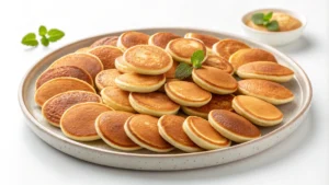 Stack of golden mini pancakes topped with syrup, berries, and powdered sugar.